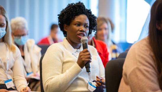 A woman with short black hair asking a question into a microphone.